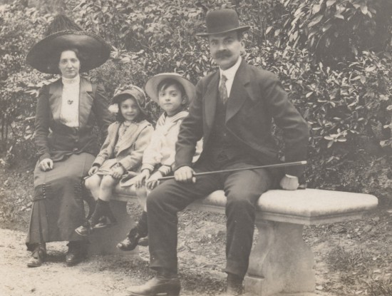 Een portret van het gezin Lamour. Angèle Plouvier zit links en Georges Lamour rechts op een bankje. Tussen hen in zitten hun twee kinderen.